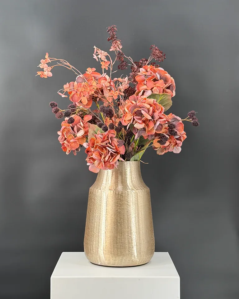 Ambra, een asymmetrisch boeket in terracotta en bordeaux in een goudkleurige vaas.