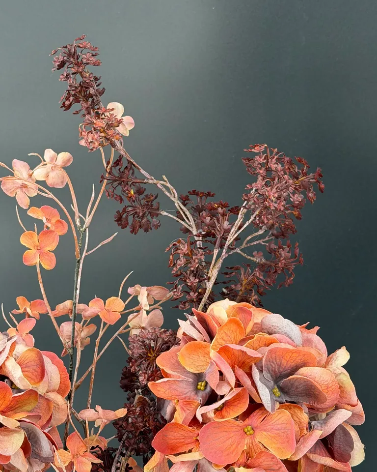 Donkere bordeauxrode bloemtakken boven de oranje hortensia’s van Ambra.
