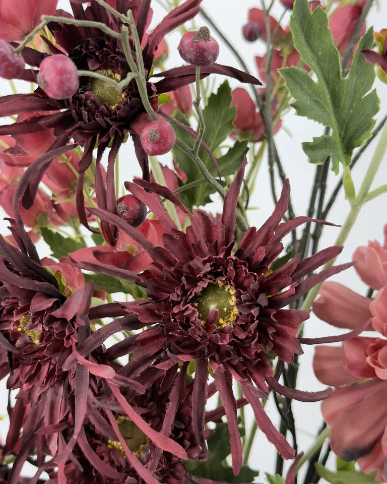 Detail van donkere bordeaux bloemen met bessen, takken en groen blad in boeket Liora.