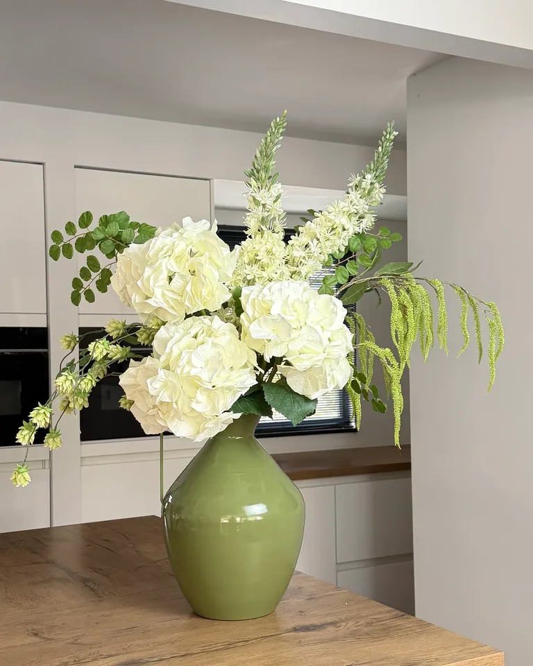 Crème-groen boeket Nerine met grote hortensia’s in een groene vaas op een houten tafel.