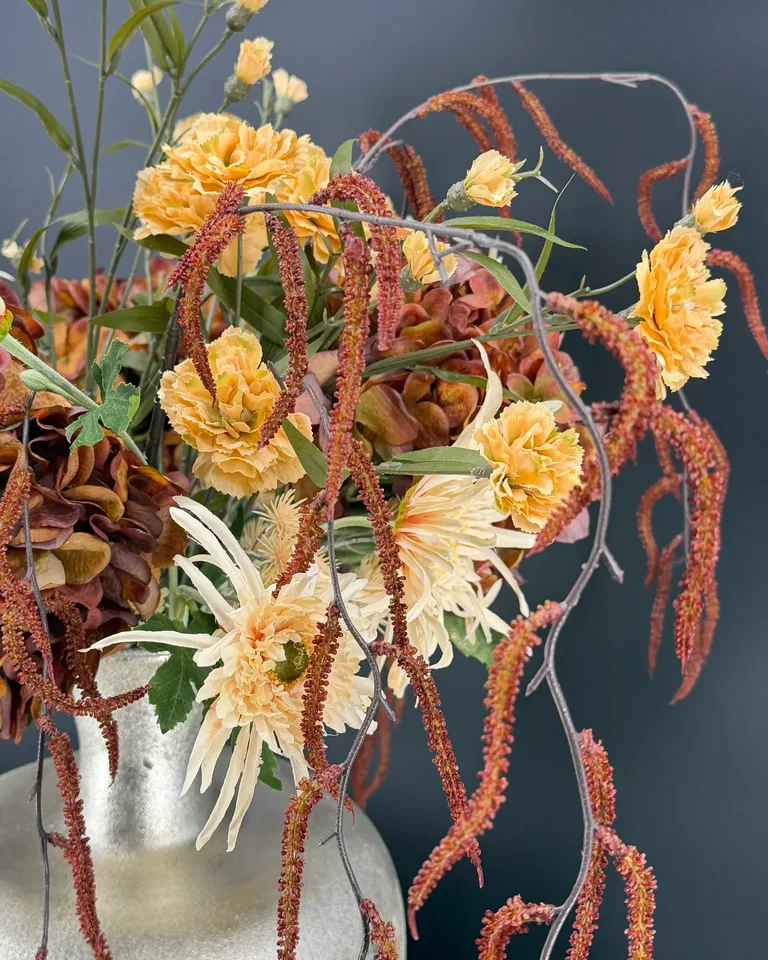 Zijaanzicht van Carmela met crèmekleurige chrysanten en loshangende bruine corylistakken.