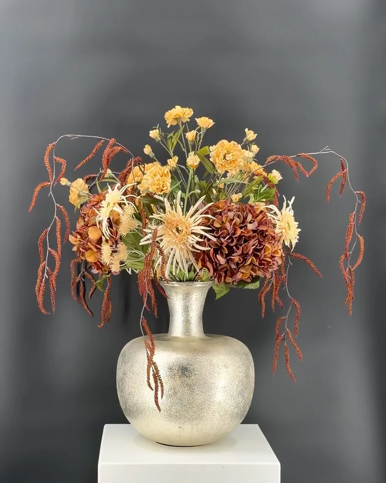 Carmela boeket met bruine hortensia’s, crèmekleurige chrysanten en corylistakken in een zilveren vaas.