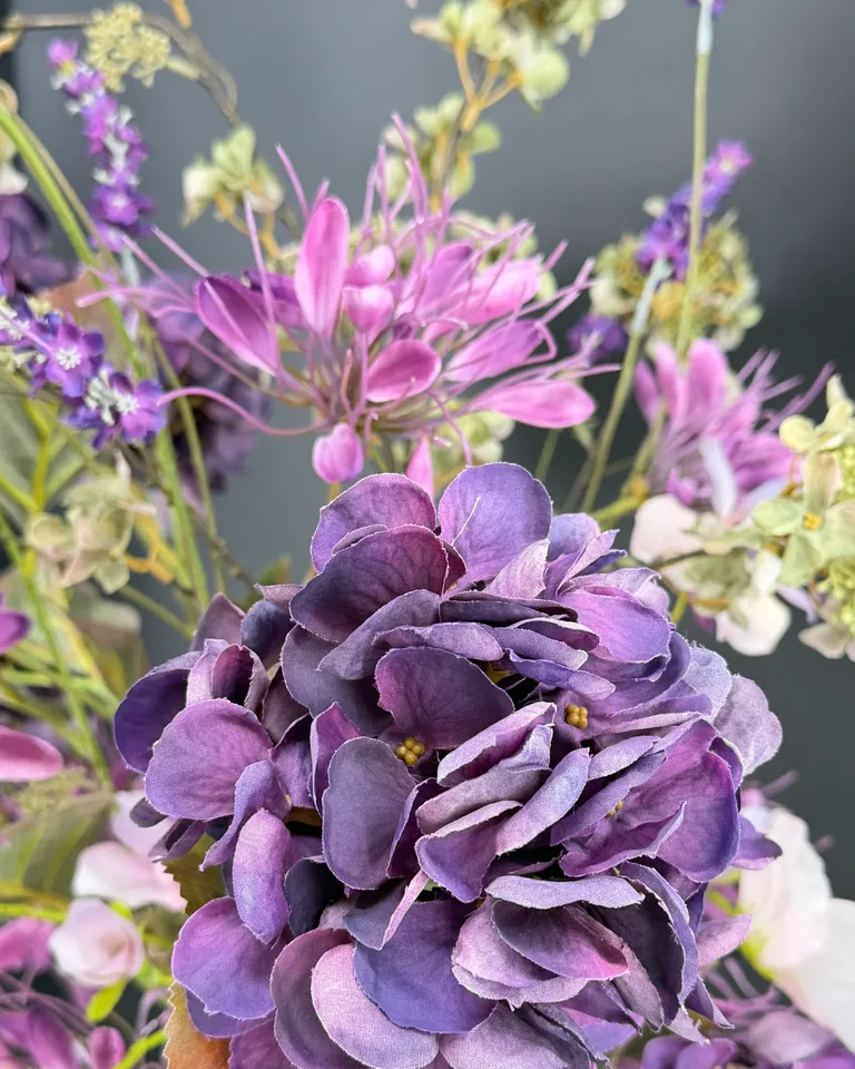Detail van paarse hortensia en roze bloemen met groene bladeren.