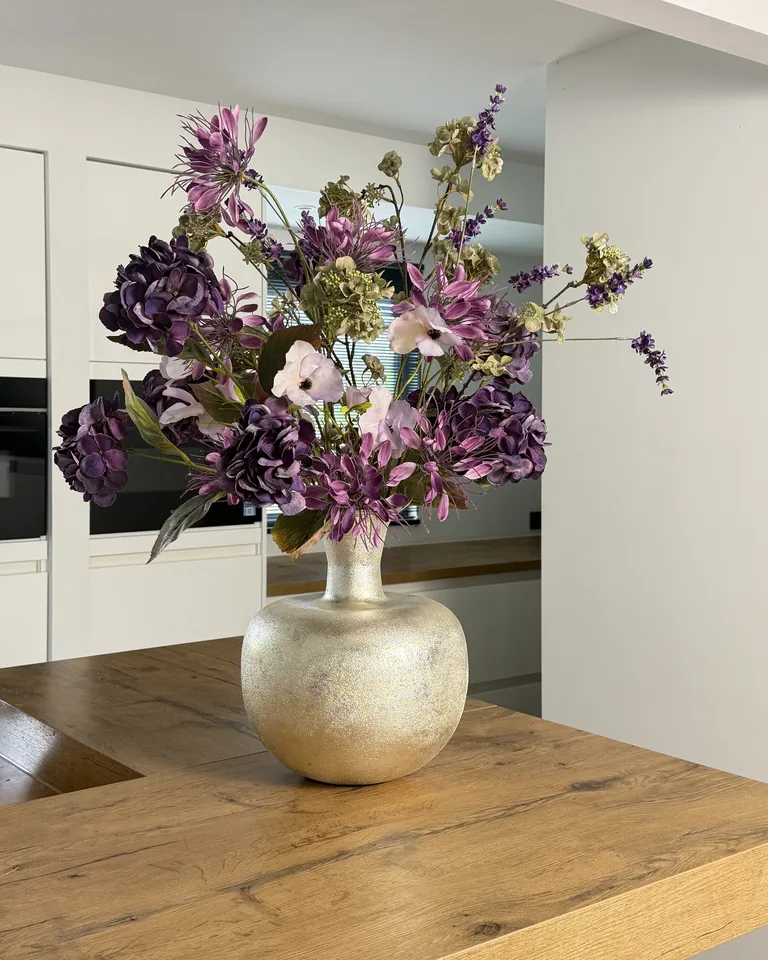 Paars-roze veldboeket met hortensia, lavendel en roze bloemen in een vaas op een houten tafel.