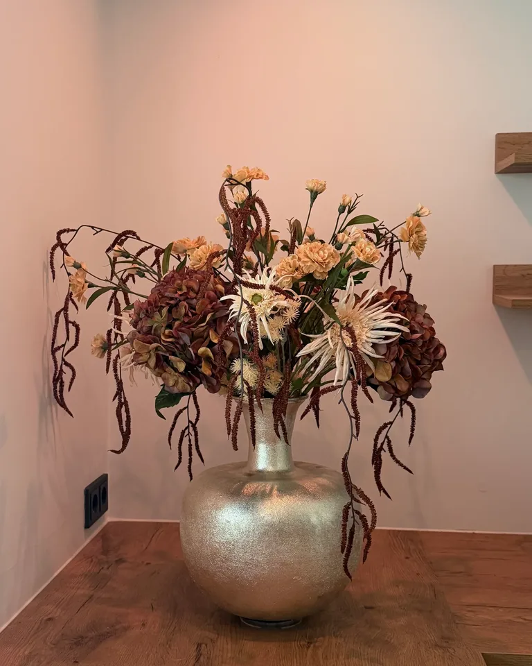 Boeket Bruna in een goudkleurige vaas op een houten blad tegen een warme wand.