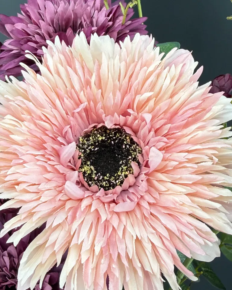 Close-up van een lichtroze dahlia in boeket Lunara, met paarse bloemen op de achtergrond.