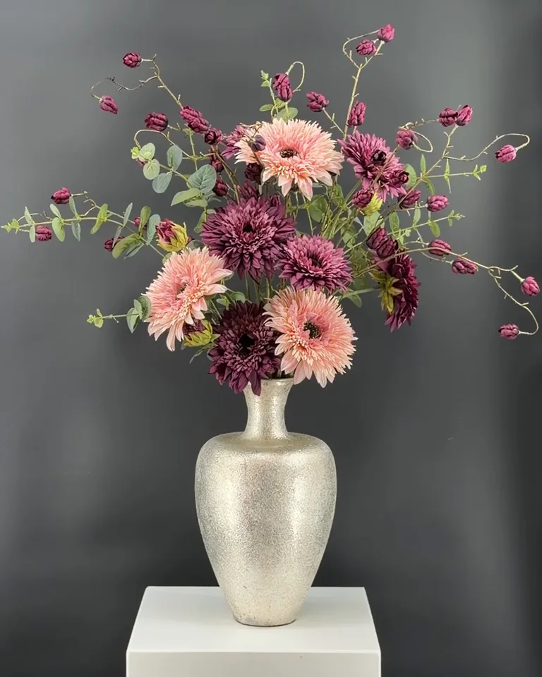 Opgaand paars-roze boeket Lunara met dahlia’s, paarse takken en eucalyptus in een goudkleurige vaas op een witte zuil.