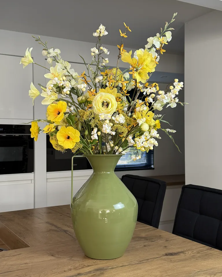 Zelora, een vol geel-wit veldboeket met gele bloemen, witte bloesem en losse takken in een groene vaas.