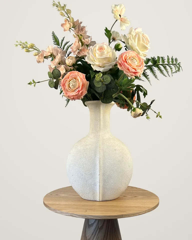 Aveline met peach en crèmekleurige bloemen in een lichte vaas op een houten bijzettafel.