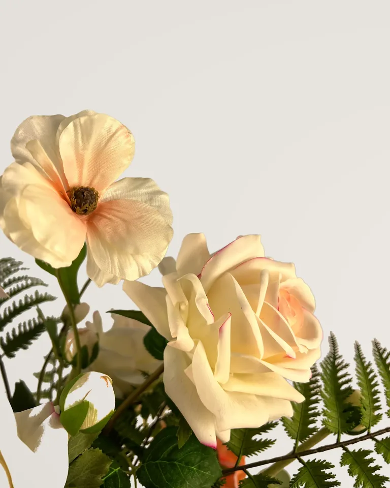 Een crèmekleurige roos naast een open lichte bloem en varenblad, van dichtbij in Aveline.