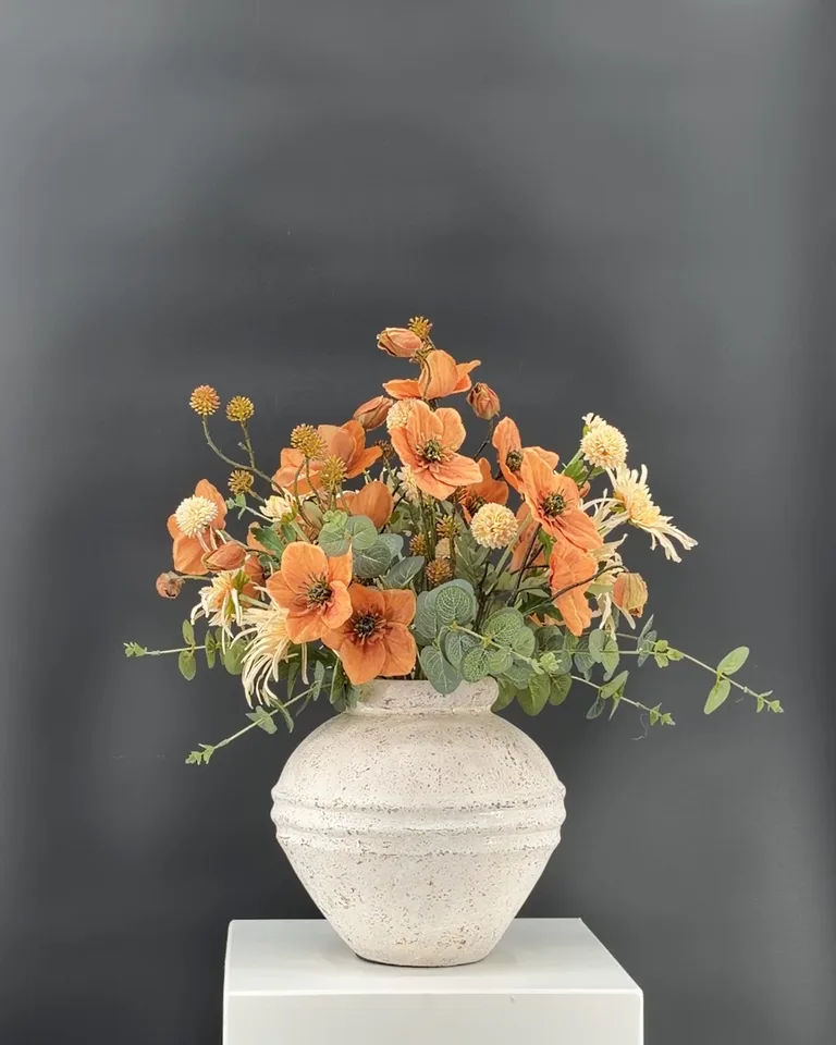 Solenne, een luchtig veldboeket in terracotta en crème met eucalyptus, in een witte ronde vaas tegen een donkere achtergrond.