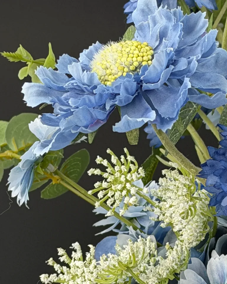 Detail van een lichtblauwe bloem met geel hart en witte bloemtakken in het blauwe boeket