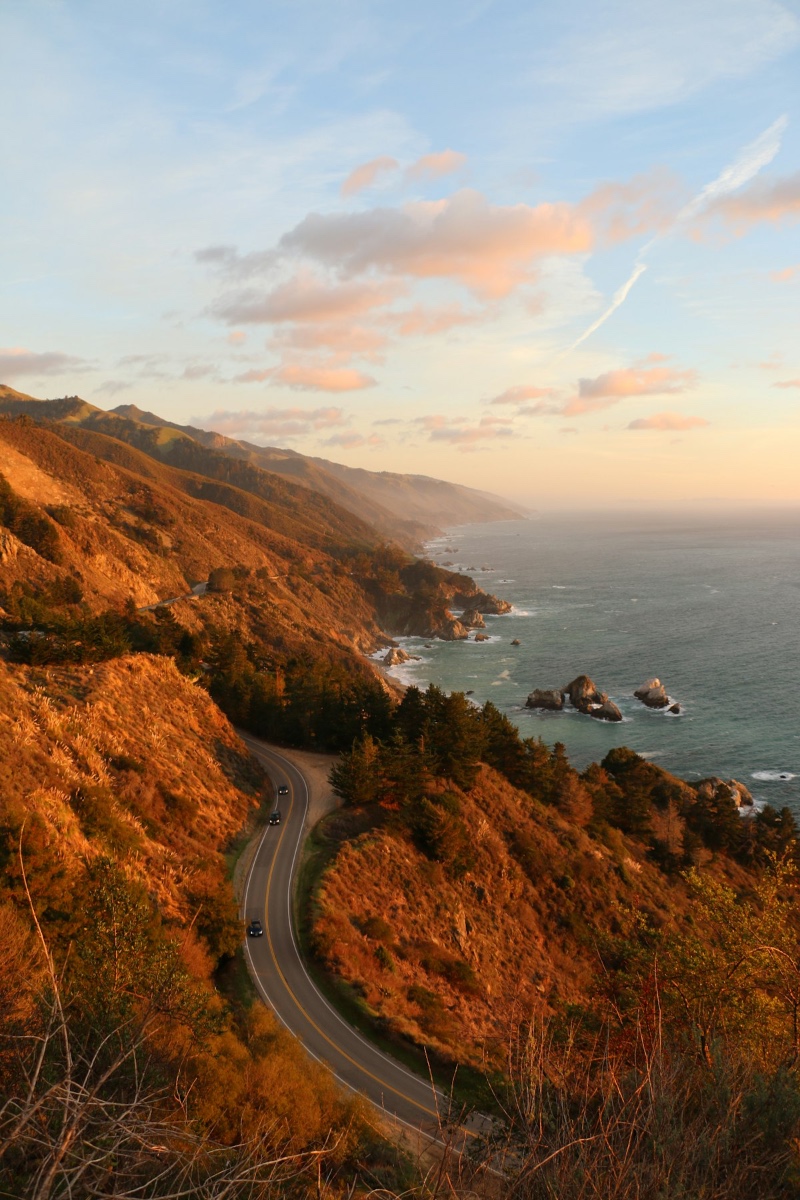 Highway 1 winding along dramatic golden coastal cliffs above the Pacific Ocean at sunset