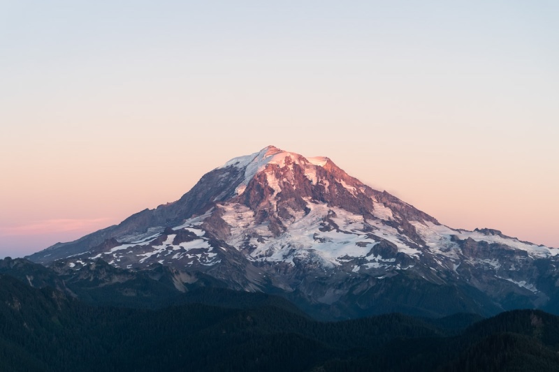 Snow-capped Mount Rainier at sunset against a soft pink and blue sky
