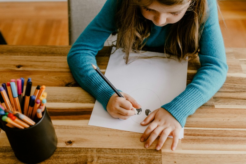 A young girl is sitting at a desk and drawing