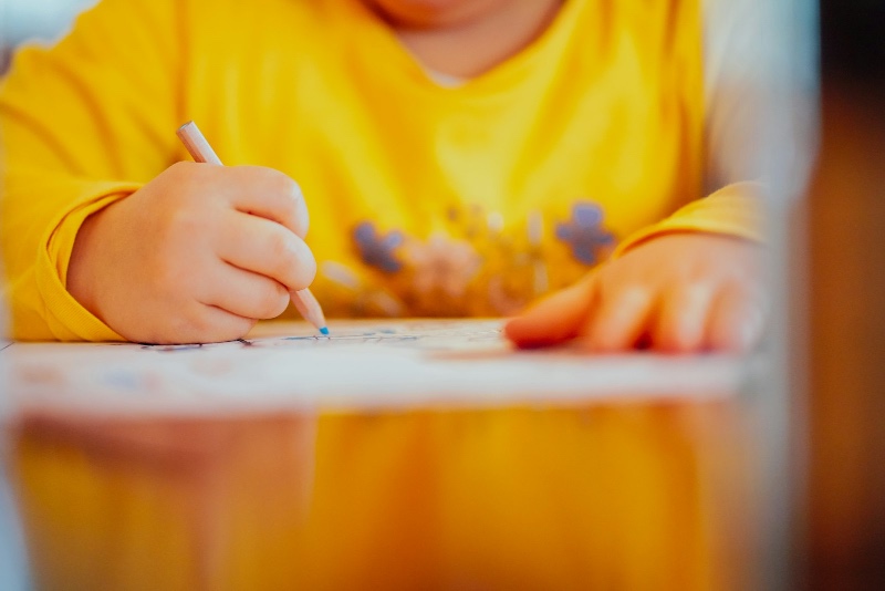 Close-up of a young child's hand drawing with a colored pencil on paper