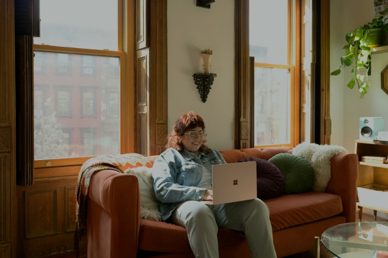 A woman sitting on a couch in an apartment using their computer for telehealth therapy