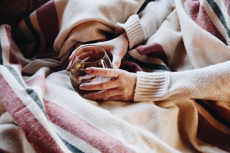 Hands wrapped in a cozy plaid blanket cradling a small glass of warm tea