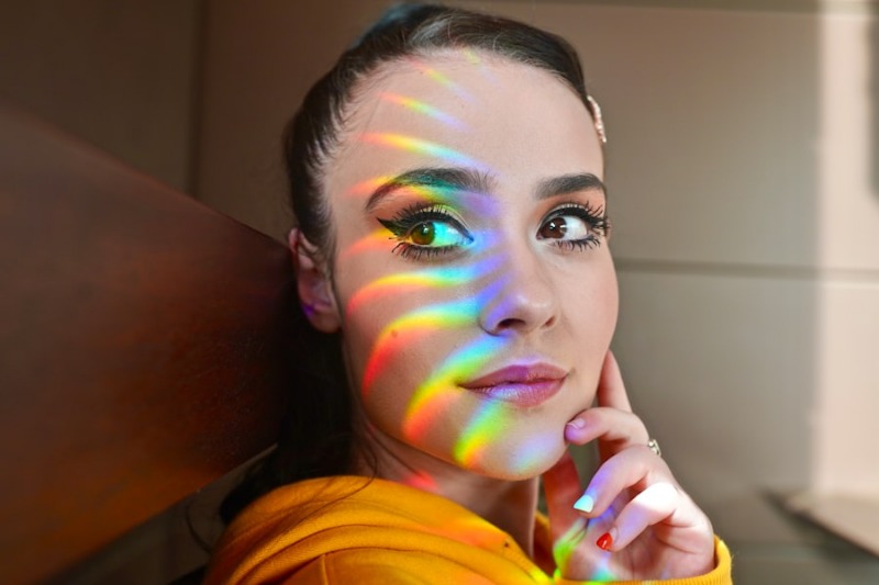 A close portrait of a woman with rainbow prism light sweeping across her face as she looks upward