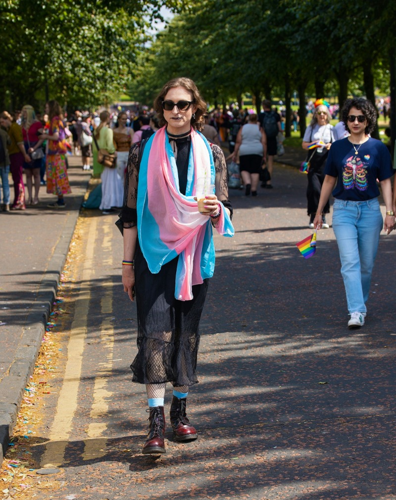 A person wearing a transgender pride flag as a scarf, walking at an outdoor event