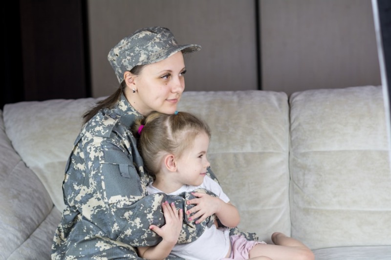 A parent in military uniform sitting on a sofa holding their young child