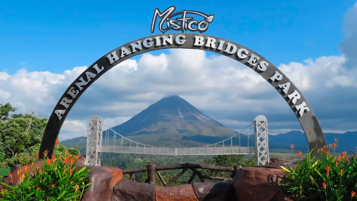Entrance sign of Mistico Arenal Hanging Bridges Park with Arenal Volcano and a scale model bridge in the background