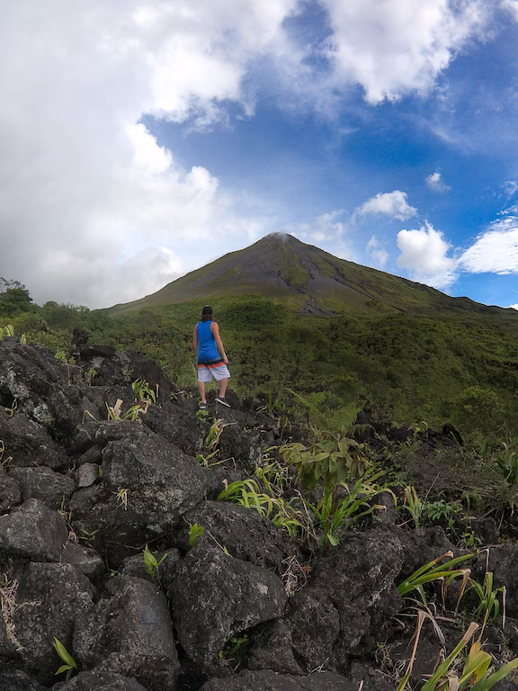 Young person standing on volcanic rock with Arenal Volcano in the background.