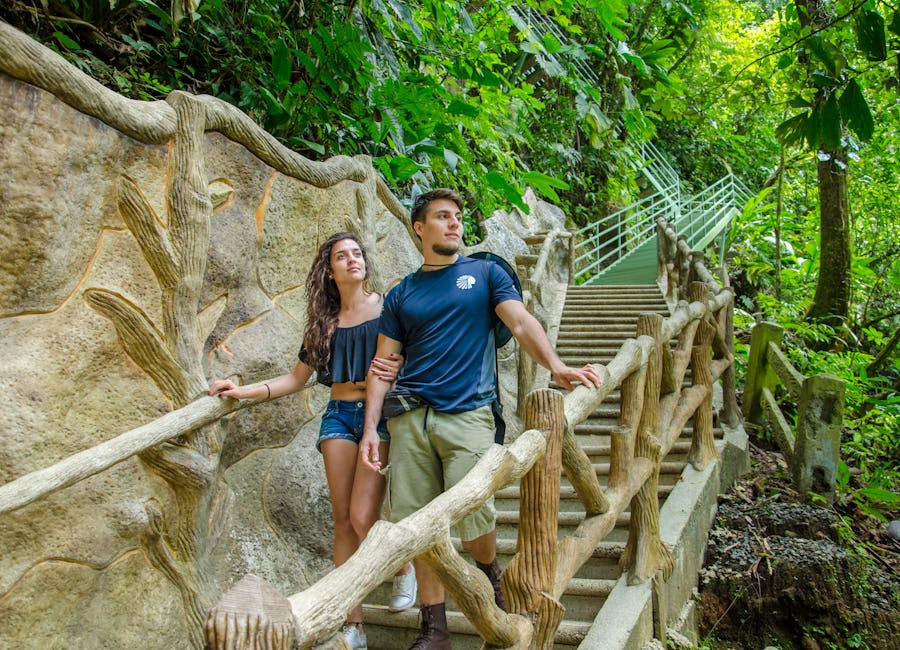 Young couple walking down stairs surrounded by lush vegetation in La Fortuna Waterfall Reserve, Costa Rica
