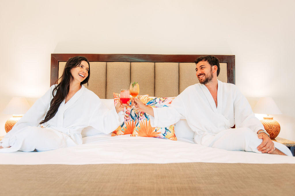 Happy couple in robes on the bed in Forest Deluxe with Jacuzzi, toasting with cocktails at Hotel & Spa Poco a Poco, Monteverde