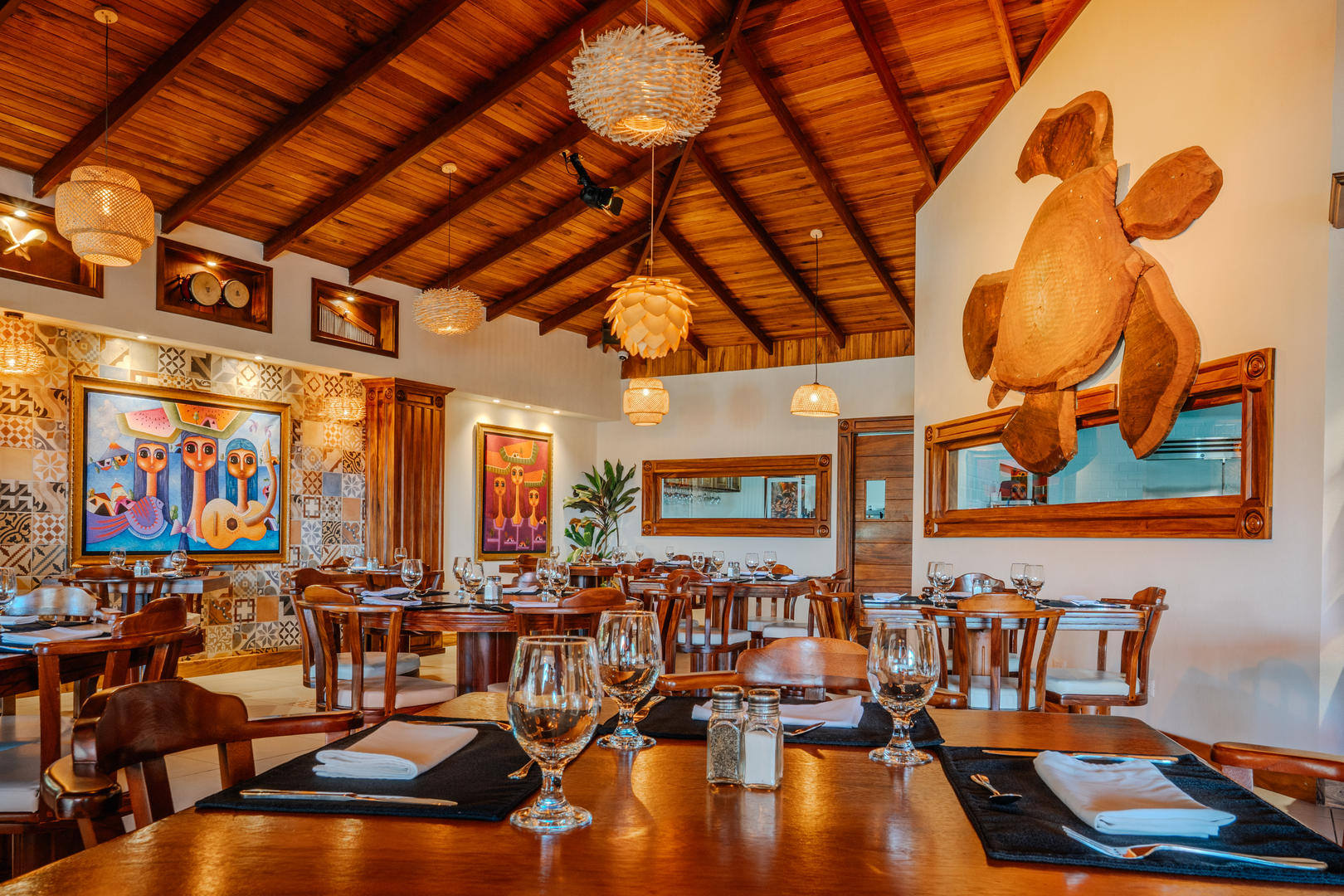 Table setting with wine glasses and decorative giant wooden turtle wall art in the background at Otocuma Restaurant, Hotel & Spa Poco a Poco, Monteverde