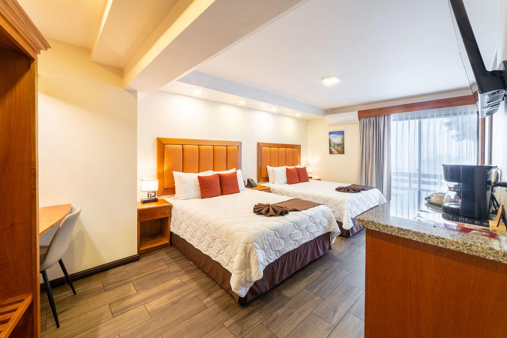 Side view of two queen beds in Quetzal Room with coffee table and exterior window at Hotel & Spa Poco a Poco, Monteverde