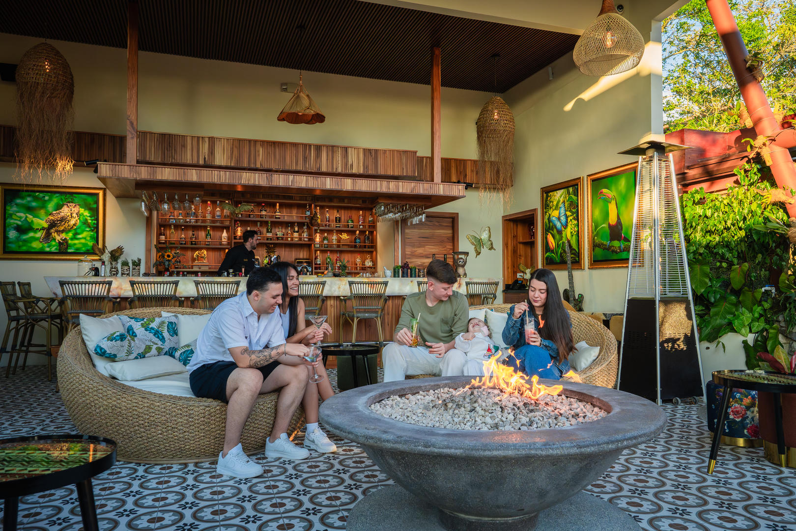 Family enjoying drinks at the bar with liquor display in the background and a fire pit in the foreground at Hotel & Spa Poco a Poco, Monteverde