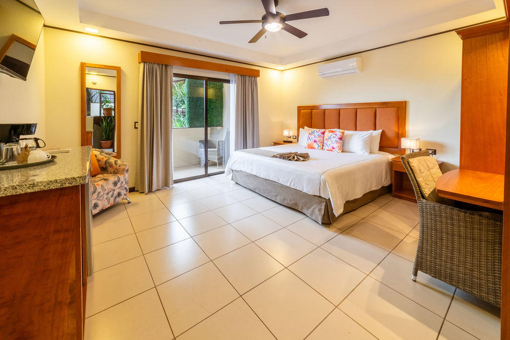 Bromelia Room corner view with a king bed, amenities, and balcony in the background at Hotel & Spa Poco a Poco, Monteverde
