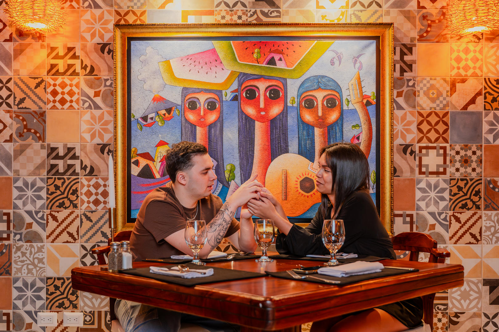 Romantic dinner couple holding hands at a table with wine glasses and elegant artwork in the background at Otocuma Restaurant, Hotel & Spa Poco a Poco, Monteverde