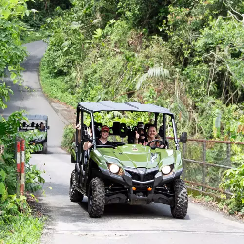 Family crossing a bridge in a side by side UTV waving at the camera with another UTV approaching behind in La Fortuna, Costa Rica