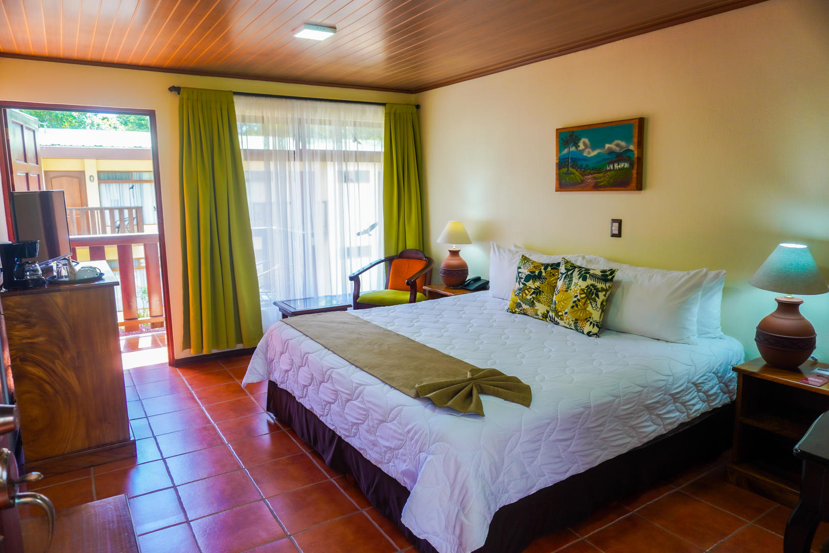 Superior room with king bed, amenities, TV, chair, and balcony view in the background at Monteverde Country Lodge, Monteverde, Costa Rica