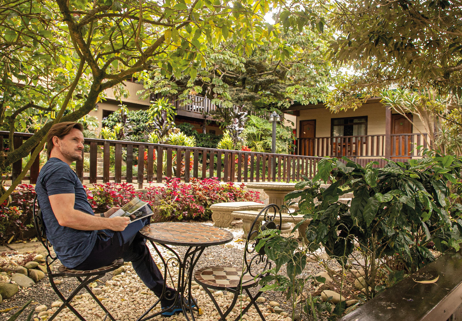 Man reading a book at an outdoor table in the hotel gardens at Monteverde Country Lodge, Monteverde, Costa Rica