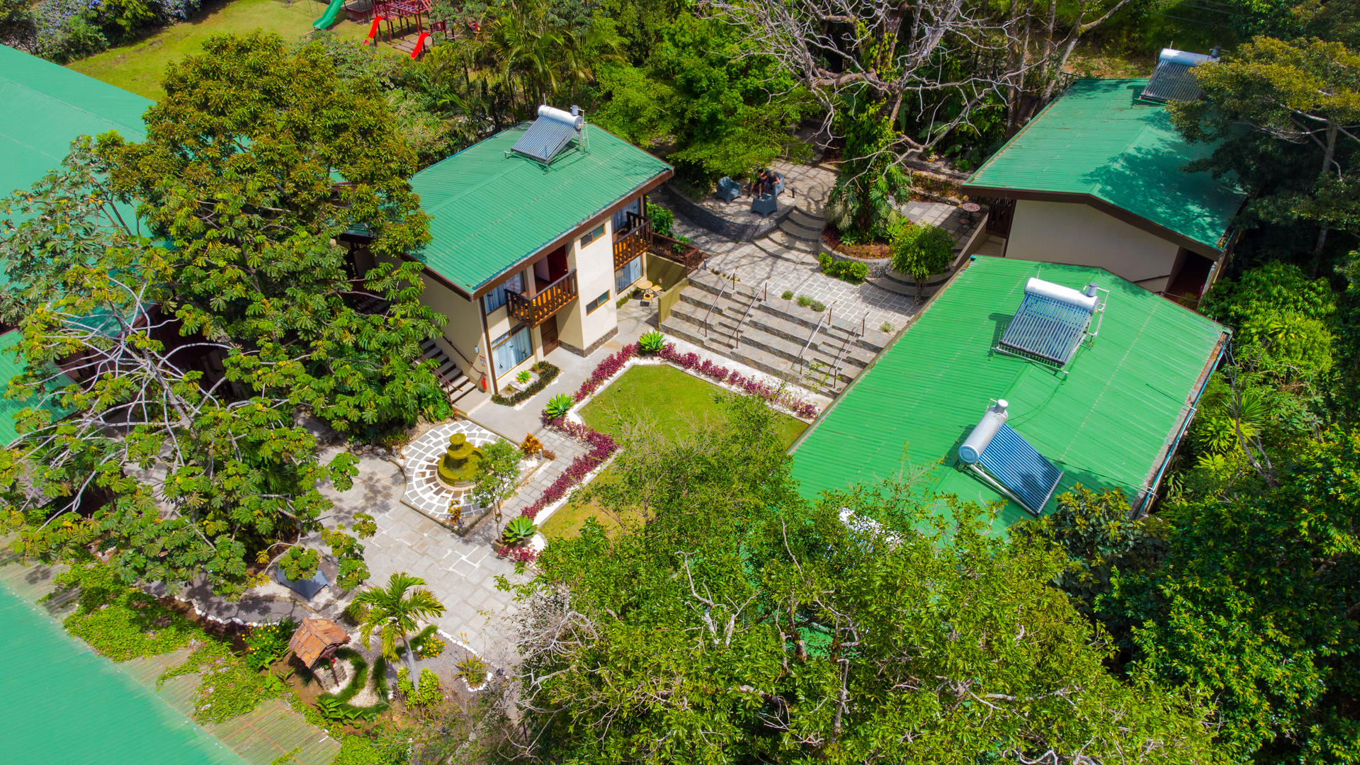Aerial view of hotel buildings connected by gardens and natural common areas, with solar panels visible on rooftops at Monteverde Country Lodge, Monteverde, Costa Rica