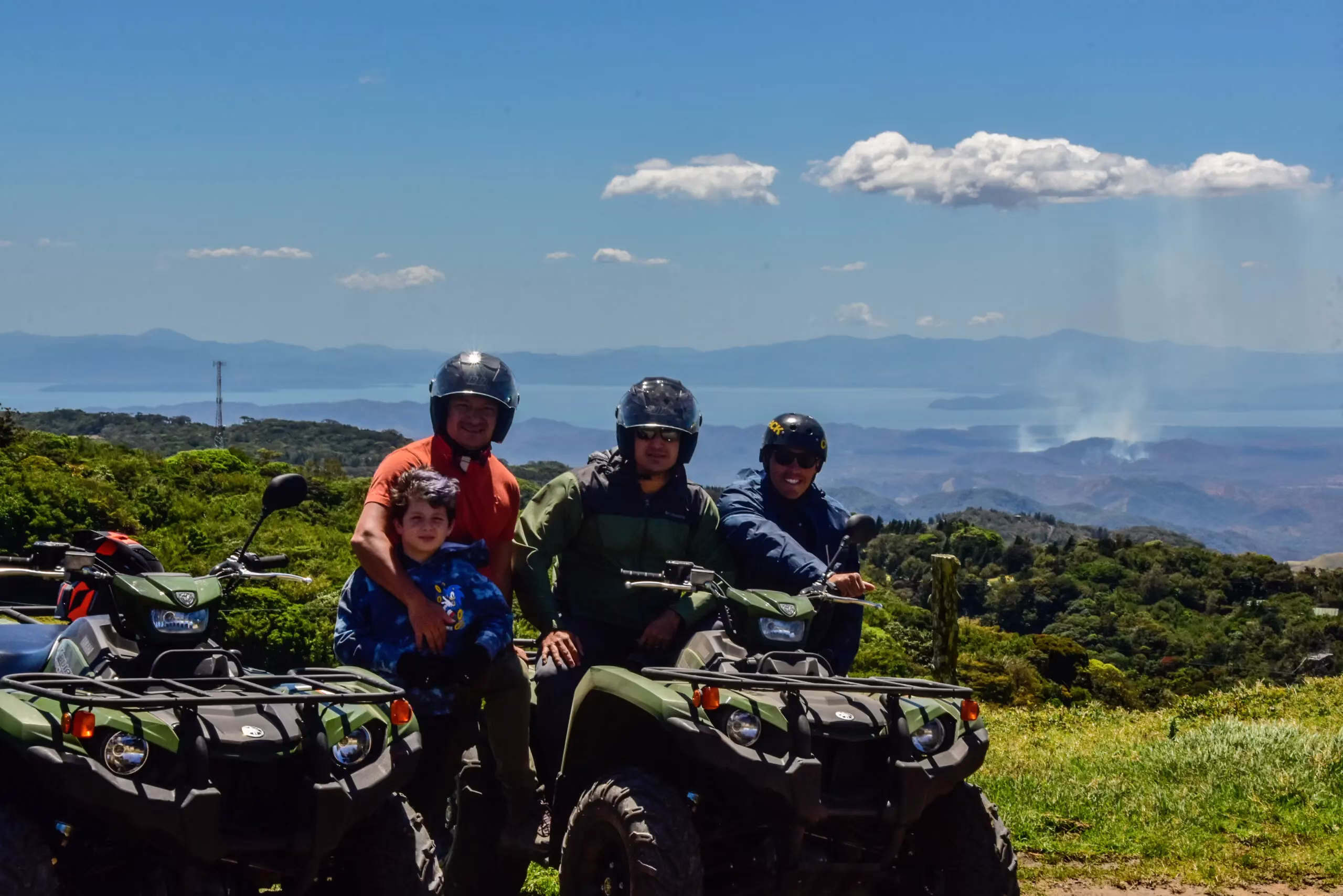 Family riding ATVs posing with Lake Arenal in the background near Monterrey viewpoint in La Fortuna, Costa Rica