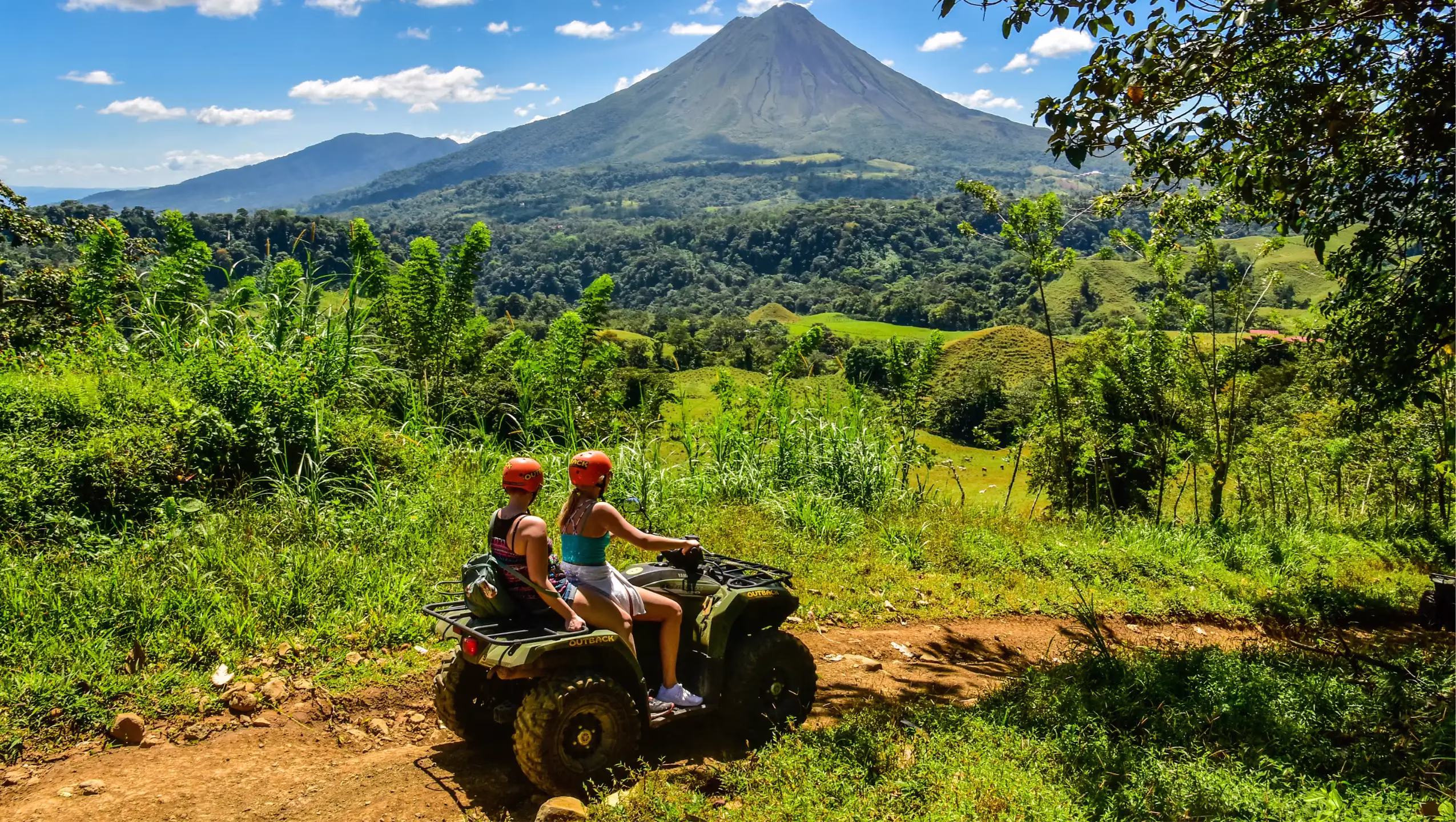 Couple posing on ATVs with Arenal Volcano in the background during a tour in La Fortuna, Costa Rica