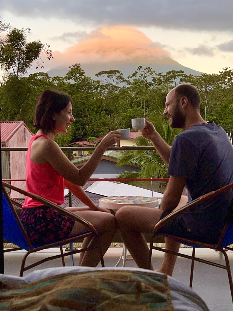 Couple toasting with coffee on a balcony with Arenal Volcano in the background at La Fortuna Lodge, La Fortuna, Costa Rica