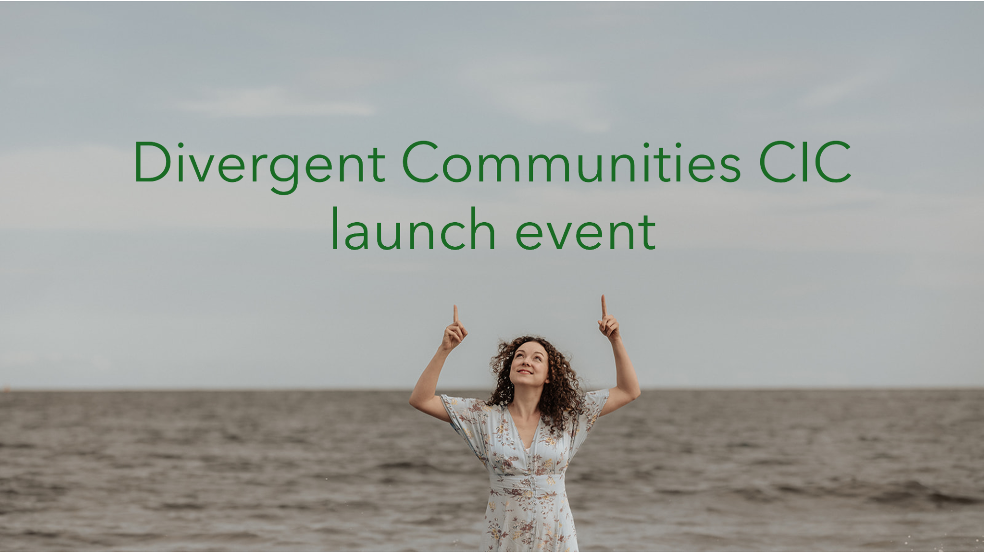 Rosie Brighty, a white woman with dark curly hair, smiling and pointing upwards at green text above her that reads “Divergent Communities CIC launch event”. The sea is in the background.