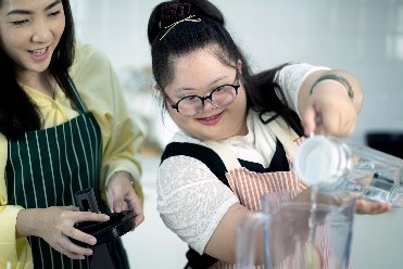 A young girl with glasses pouring water in a blender. 