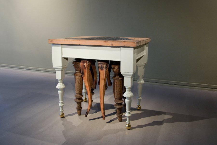 Skulpturell installasjon av Markus Lantto: et bord med utskårne treben i et utstillingsrom.