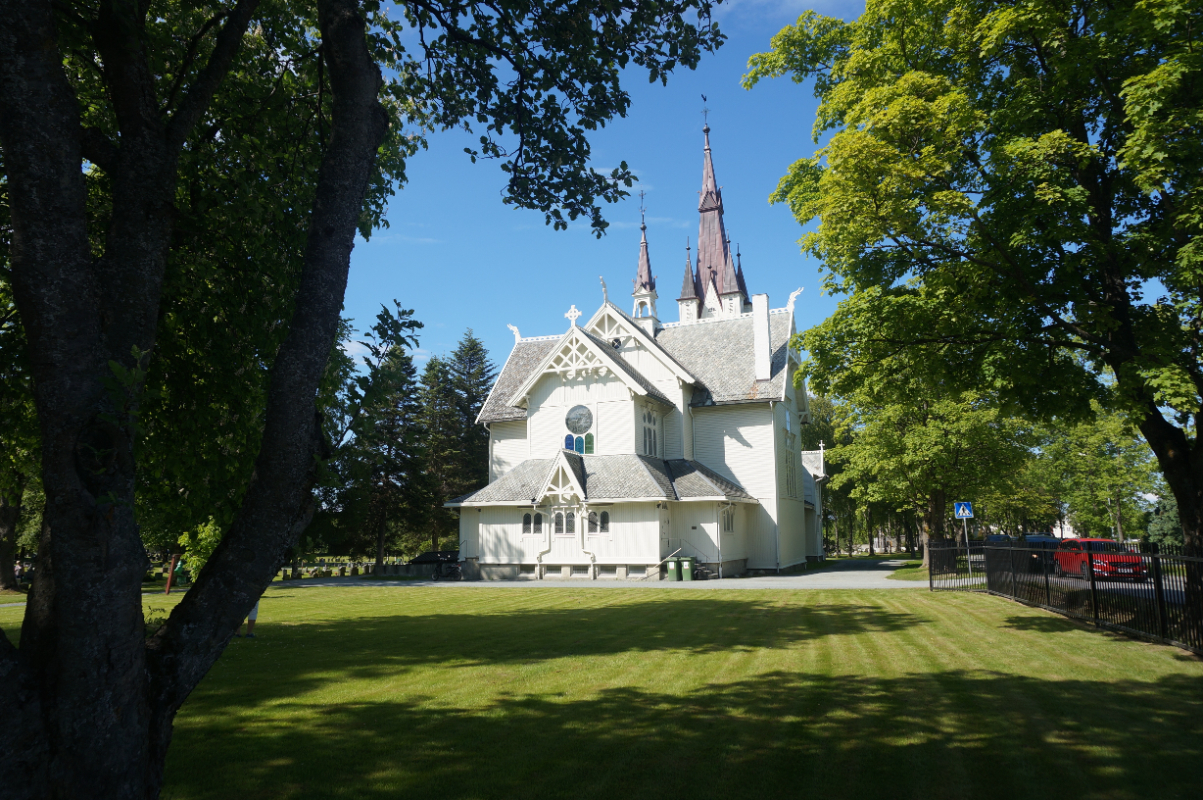 Hvit trekirke omgitt av høye trær