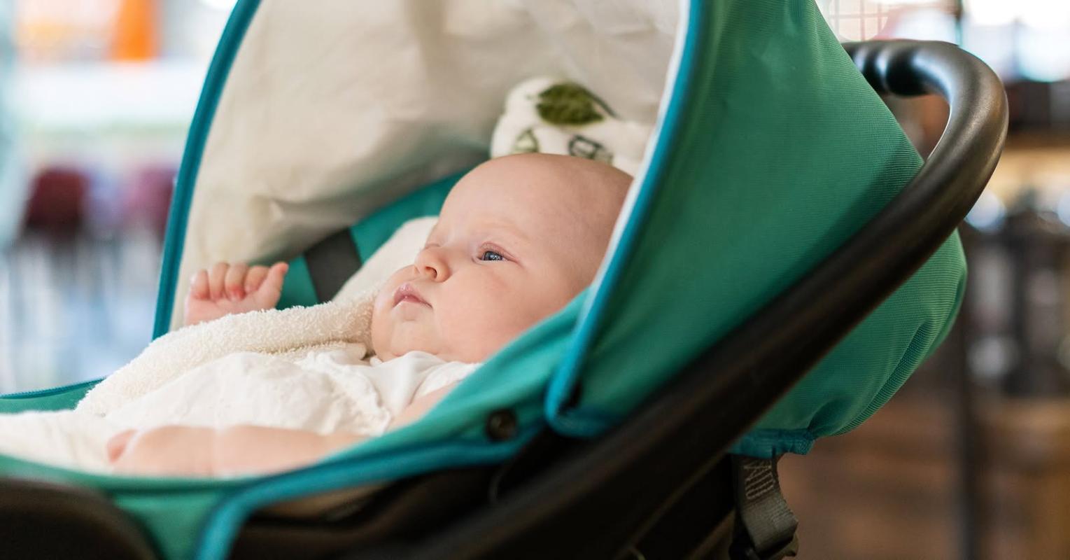 Baby ligger i barnevogn og betrakter et eller annet utenfor bildet
