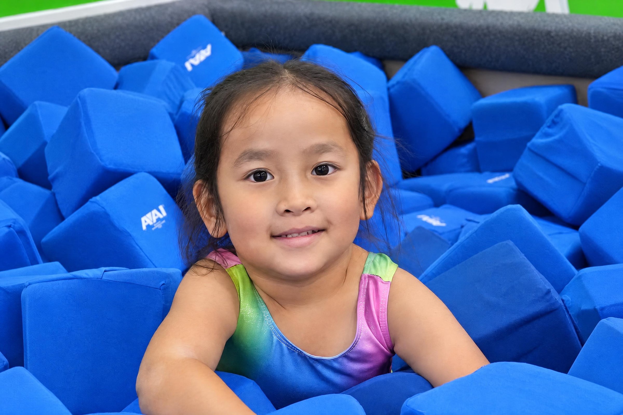 Smiling preschool girl playing in a foam pit of blue blocks