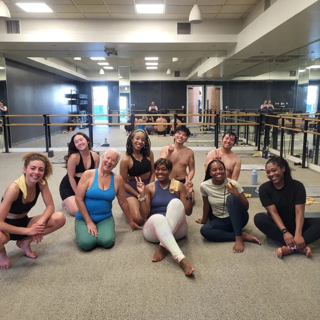 Group of yoga participants smiling together in a mirrored studio