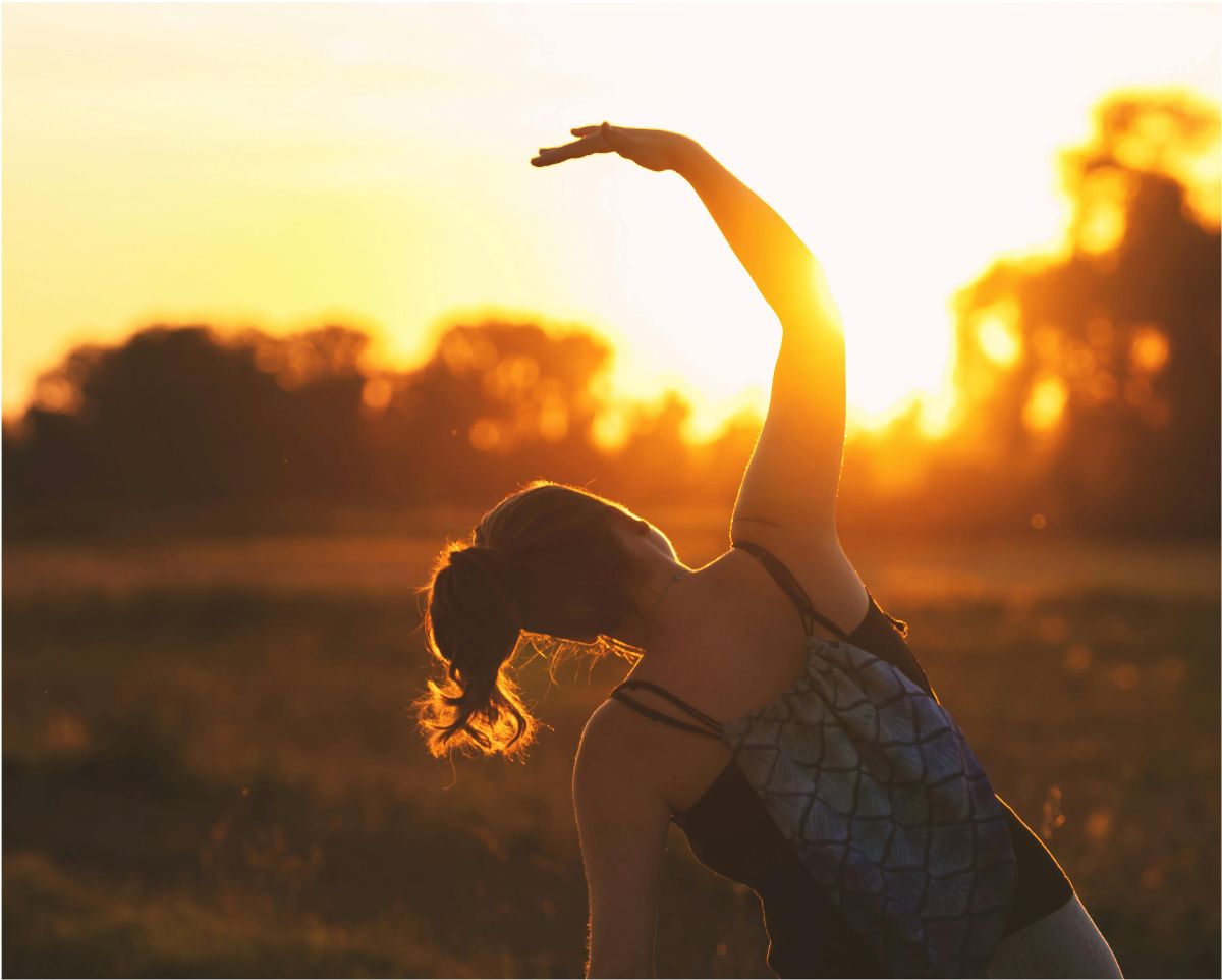 Silhouette of a woman stretching in a field at sunset