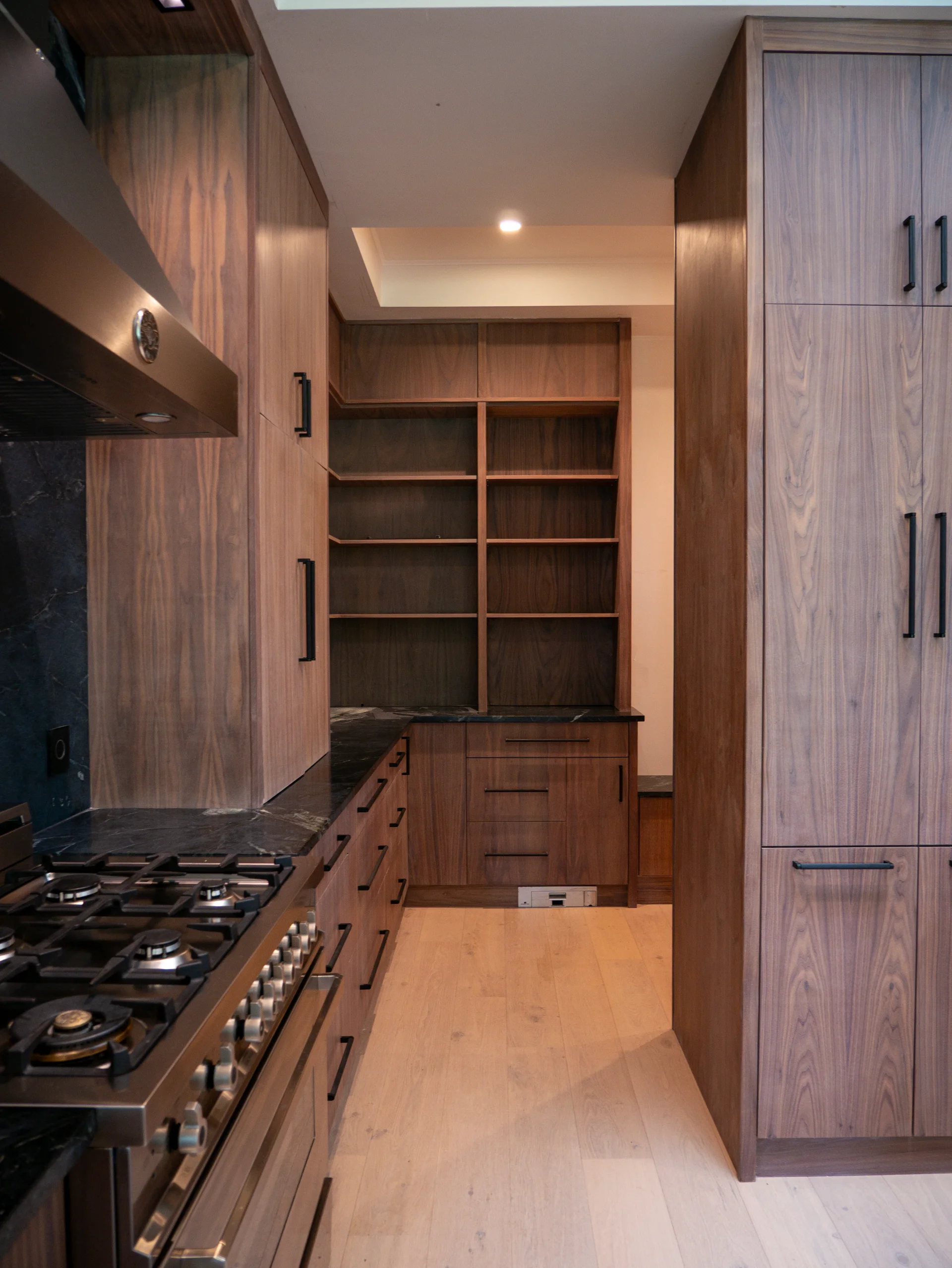 Modern grain-matched walnut kitchen in Austin, West Lake Hills, featuring a green soapstone backsplash, stainless steel range, and minimalist island cabinetry. - Detail 6